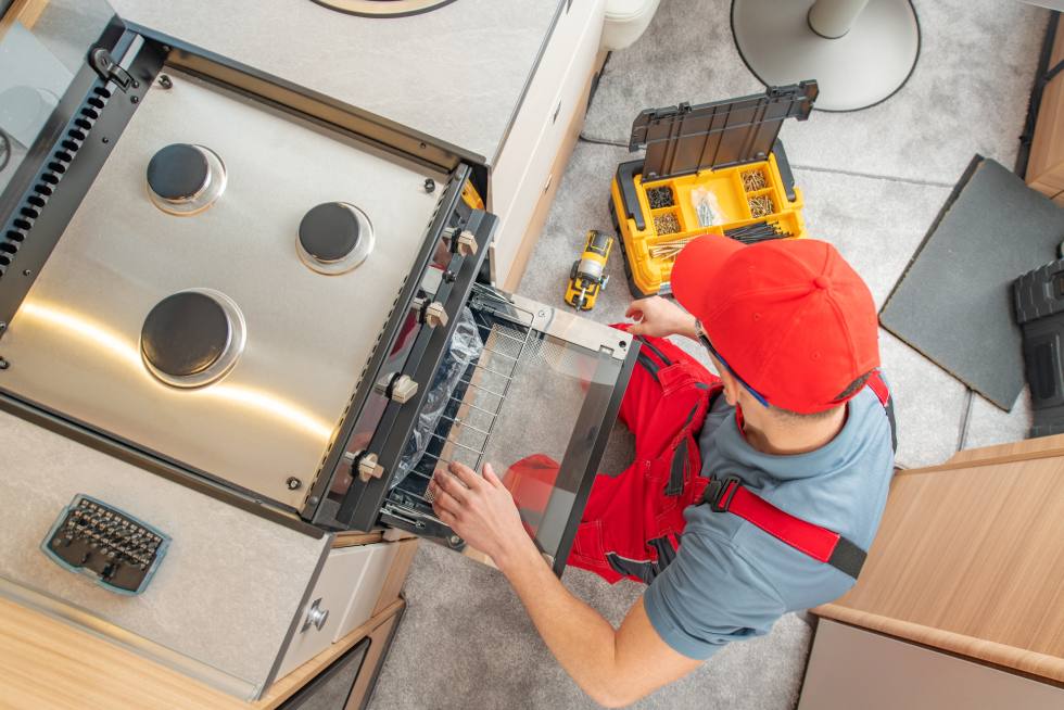 A technician in red overalls and red hat fixing an oven